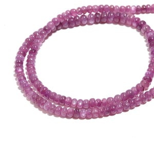 Op de afbeelding: Een ketting bestaande uit kleine, ronde, roze edelstenen. De kralen zijn aan elkaar geregen en vormen een delicate streng. De edelstenen hebben een gepolijste uitstraling en een consistente kleur.