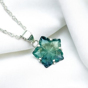 May include: A silver necklace featuring a six-pointed star pendant. The pendant has a blend of blue and green colours. The necklace is presented against a white backdrop.
