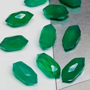 Op de afbeelding: Een verzameling van tien gefacetteerde groene edelsteen kralen, waarschijnlijk voor het maken van sieraden, getoond op een zilveren dienblad.
