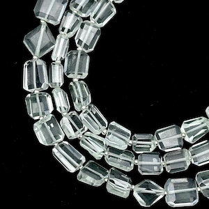 Może przedstawiać: Szereg fasetowanych koralików z jasnozielonego kamienia szlachetnego. Koraliki są prostokątne i mają delikatny połysk.