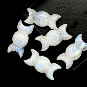 May include: Five moon-shaped, carved gemstone pendants. The pendants are white with blue and iridescent flashes. The pendants are arranged on a black surface.