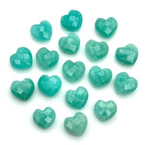 以下が含まれることがあります： さまざまなティールとターコイズの色合いの、ファセット加工されたハート型の宝石のコレクション。宝石は白い背景に配置され、磨かれた表面とユニークな形状が示されています。ジュエリー作りや工芸に最適です。