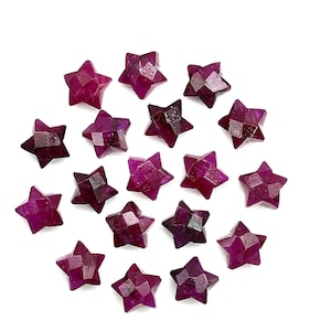 Könnte beinhalten: Eine Sammlung von 16 sternförmigen Rubinen, jede mit einem tiefen Rotton und einer facettierten Oberfläche. Die Edelsteine sind in einem Kreis auf weißem Hintergrund angeordnet.