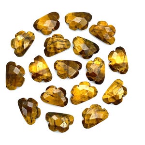 Pode incluir: Uma coleção de pedras preciosas facetadas de olho de tigre, cada uma com uma forma única de nuvem. As pedras exibem uma mistura de tons marrom dourado e marrom escuro, com chatoyancy visível. As pedras preciosas estão dispostas em um fundo branco.