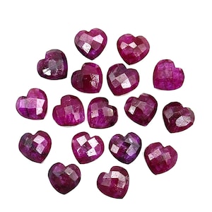 Op de afbeelding: Een verzameling gefacetteerde, hartvormige edelstenen in verschillende tinten diep rood en paars. De edelstenen zijn verspreid op een witte achtergrond, waardoor hun gepolijste oppervlakken en unieke vormen worden benadrukt.