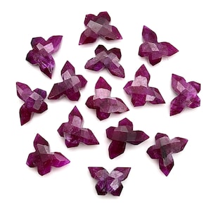 May include: A collection of faceted, butterfly-shaped gemstones in varying shades of deep magenta and purple. The gemstones are arranged on a white background, showcasing their intricate cuts and natural color variations. These gemstones are ideal for jewelry making.