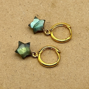 May include: Gold hoop earrings with a star-shaped labradorite gemstone pendant. The earrings are a light gold color and the labradorite is a dark green with iridescent blue and green flashes.
