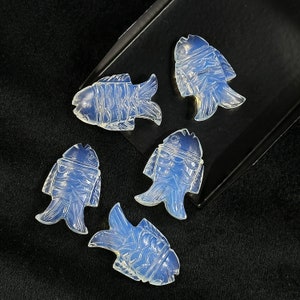 May include: Five white opal fish carvings, each with a unique design, are displayed on a black surface. The carvings are detailed and intricate, showcasing the beauty of the opal.