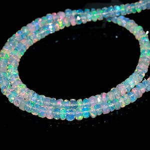 May include: Strands of iridescent opal beads. The beads are a mix of white, pink, blue, and green, with a faceted cut that catches the light. The beads are strung together, creating a necklace or bracelet.