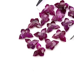 May include: A selection of star-shaped gemstones, cut with multiple facets, in deep magenta and purple hues. The gemstones are arranged on a white background, highlighting their geometric shapes and reflective qualities. The image conveys a sense of luxury and natural elegance.