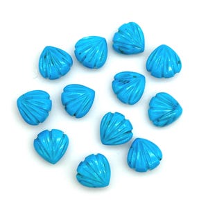 May include: A collection of turquoise-colored, shell-shaped beads. Each bead has a detailed carved design, with grooves radiating from the center. The beads are arranged on a white background, showcasing their vibrant blue hue and intricate details.