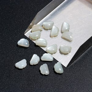 Op de afbeelding: Een verzameling witte, iriserende, schelpvormige kralen. De kralen zijn gerangschikt op een metalen dienblad.