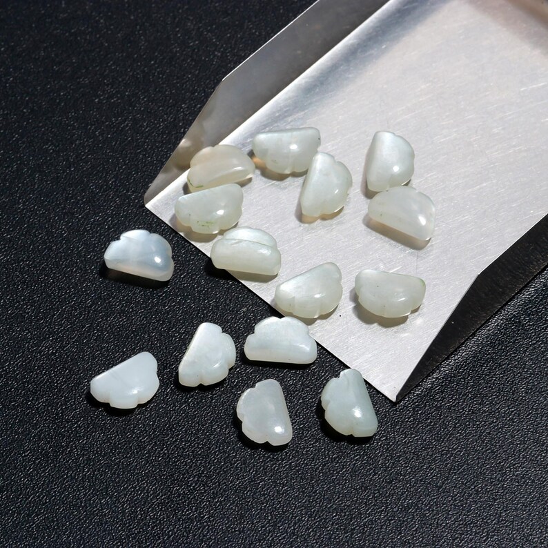 Op de afbeelding: Een verzameling witte, iriserende, schelpvormige kralen. De kralen zijn gerangschikt op een metalen dienblad.