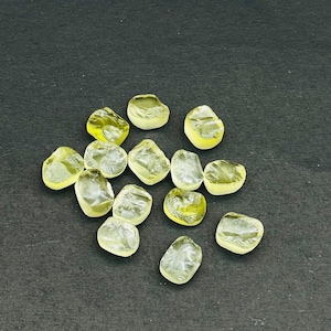 May include: A collection of 13 yellow-green faceted gemstones, likely citrine, displayed on a black surface.