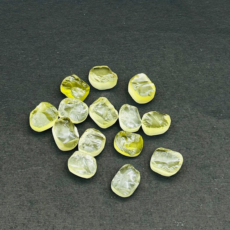 May include: A collection of 13 yellow-green faceted gemstones, likely citrine, displayed on a black surface.