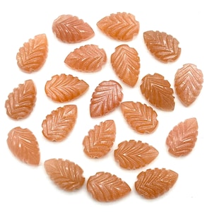 May include: A collection of 18 carved sunstone leaf shaped cabochons. The stones are a light orange color with a shimmery finish.