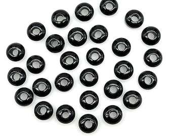 May include: A collection of black round beads with a hole in the center. The beads are scattered on a white surface.