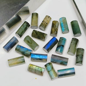 May include: A collection of 18 faceted labradorite gemstone beads in various shades of green, blue, and gray. The beads are all rectangular in shape and have a smooth, polished finish.