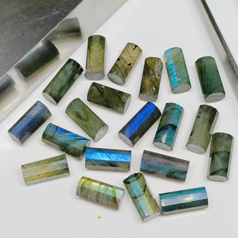May include: A collection of 18 faceted labradorite gemstone beads in various shades of green, blue, and gray. The beads are all rectangular in shape and have a smooth, polished finish.