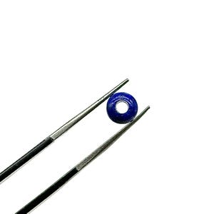 May include: A round, dark blue lapis lazuli bead with a hole in the center, held by tweezers.
