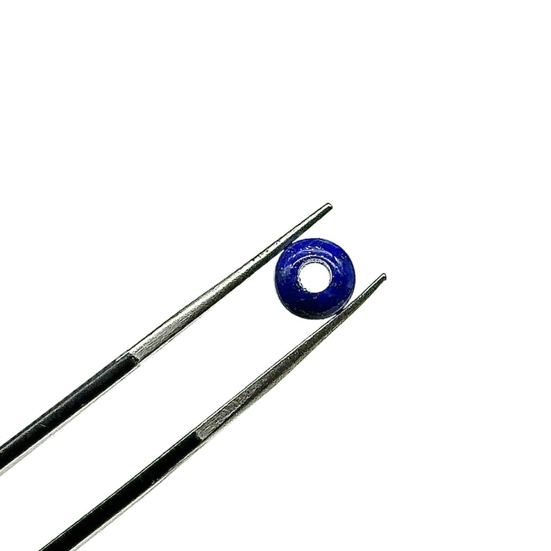 May include: A round, dark blue lapis lazuli bead with a hole in the center, held by tweezers.