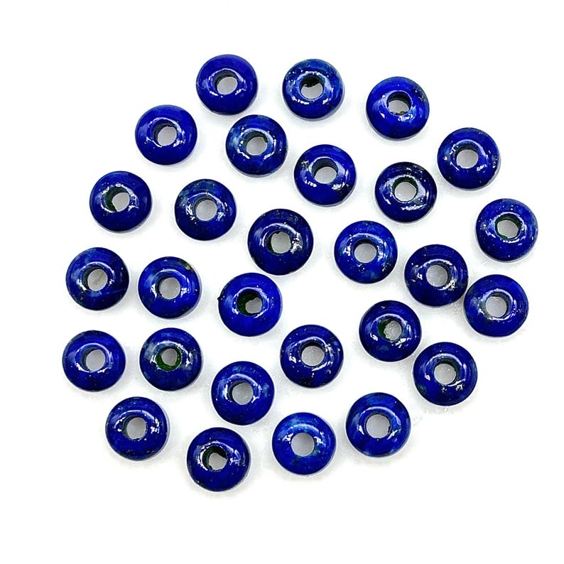May include: A collection of 25 round, dark blue lapis lazuli beads with a hole in the center. The beads are arranged in a circle on a white background.