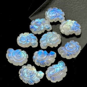 May include: Ten iridescent white moonstone cabochons carved with a swirling leaf design. The stones are approximately 2.5 cm in length and have a blue and green iridescent sheen.