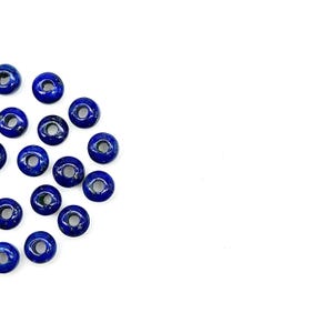 May include: A collection of round, blue lapis lazuli beads with a hole in the center. The beads are scattered on a white surface.