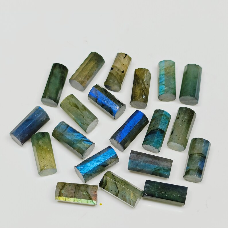 May include: A collection of 18 labradorite gemstone beads, each with a unique iridescent blue and green color. The beads are shaped like cylinders and have a smooth, polished finish.