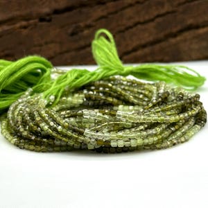 May include: A strand of green and clear faceted square beads, strung on green thread. The beads are approximately 4mm in size.