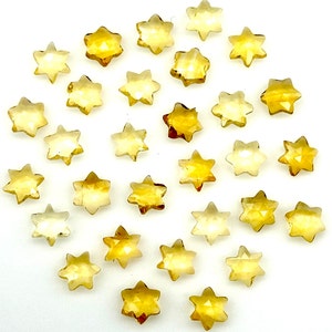 May include: A collection of 25 faceted, star-shaped, topaz gemstones. The stones are a light to medium yellow color and have a high shine.