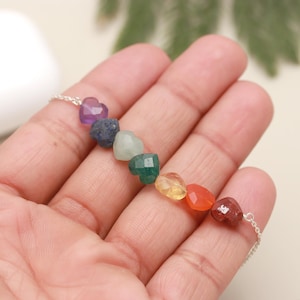May include: A silver chain necklace with seven heart-shaped gemstone beads in rainbow colors. The beads are amethyst, lapis lazuli, aventurine, emerald, citrine, carnelian, and red jasper.