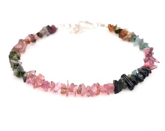 May include: A multi-colored gemstone necklace with a silver clasp. The necklace features a gradient of pink, green, and black gemstones.