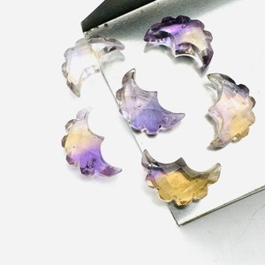 May include: Six crescent moon shaped gemstones with a gradient of purple and yellow colours. The gemstones are on a silver tray.