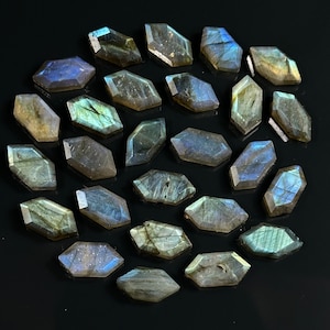 May include: A collection of 25 iridescent labradorite gemstone cabochons in a faceted, elongated hexagon shape. The stones are a mix of gray, green, and blue with a shimmery, iridescent finish.