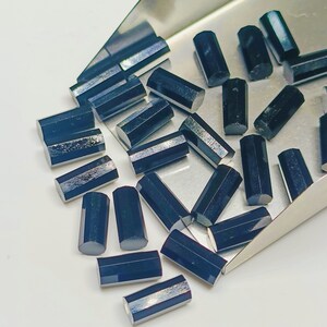 May include: A collection of black faceted gemstone beads in a metal scoop. The beads are all approximately the same size and shape, and they have a shiny, reflective surface.