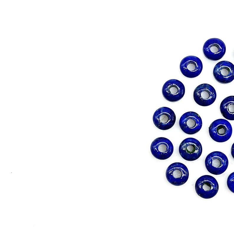 May include: A group of dark blue lapis lazuli donut beads with a hole in the center. The beads are arranged in a semi-circle on a white background.