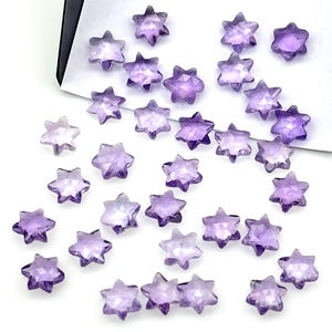 Puede incluir: Una colección de 30 piedras preciosas de amatista en forma de estrella. Las piedras son de color púrpura claro y tienen un acabado facetado.