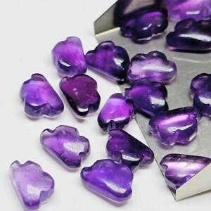 May include: A collection of purple amethyst gemstone beads in the shape of clouds. The beads are smooth and polished, with a light purple hue.