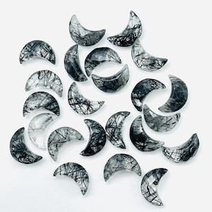 May include: A collection of 20 crescent-shaped black tourmaline gemstone cabochons. The cabochons are translucent and have a black and white color pattern.