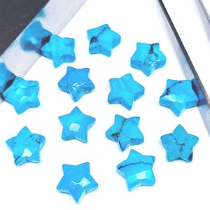 May include: A collection of turquoise star-shaped gemstones. Each star has a faceted surface and a vibrant blue colour with darker veining. The gemstones are arranged on a white surface, with a silver tool partially visible in the upper left corner.