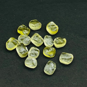 May include: A collection of 13 yellow-green gemstones, some with a slightly cloudy appearance, arranged on a black surface.