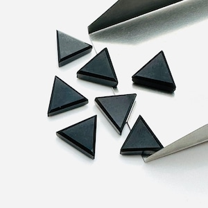 Peut inclure: Huit cabochons de pierres précieuses triangulaires noirs, probablement de l'onyx, sur un plateau argenté. Les pierres précieuses sont facettées et ont une finition lisse et polie.