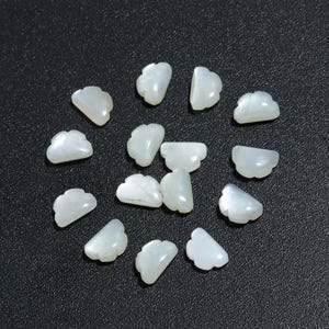 Op de afbeelding: Een verzameling witte, iriserende, schelpvormige kralen. De kralen zijn gevormd als een wolk met een gegolfde rand.