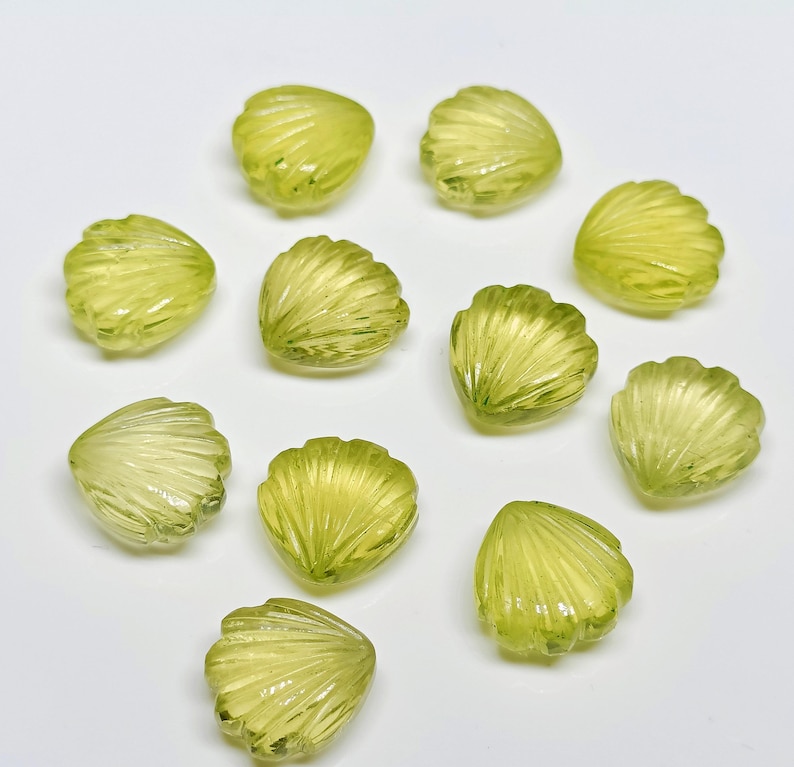 May include: A collection of 12 green gemstone shell-shaped beads. The beads are all the same size and shape, and they are arranged in a random pattern.