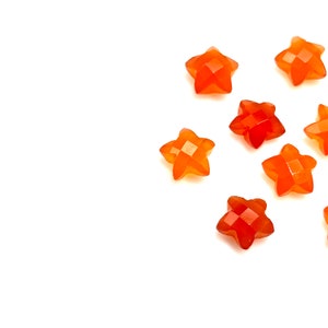 May include: A collection of eight orange star-shaped carnelian gemstones on a white background.