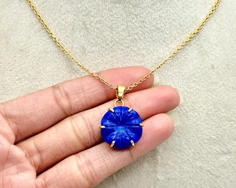 Könnte beinhalten: Eine goldene Kettenkette mit einem blauen, geschnitzten Blumenanhänger. Der Anhänger ist rund und hat ein detailliertes Design.