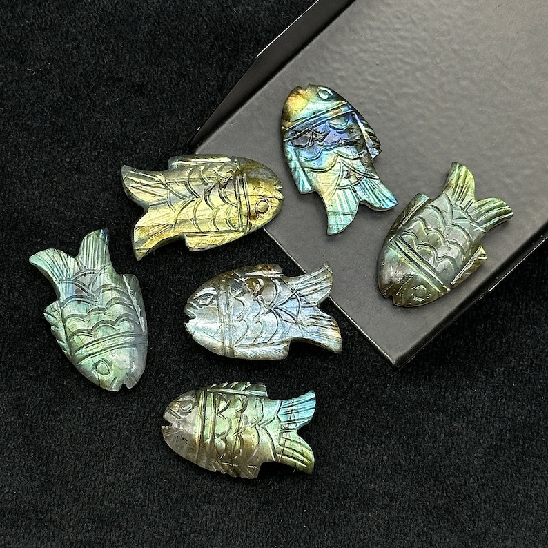 Puede incluir: Seis tallas de peces de labradorita iridiscente. Los peces est&aacute;n tallados en un estilo realista detallado y tienen una variedad de colores, incluyendo verde, azul y dorado.