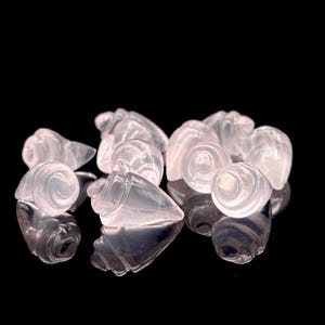 May include: A group of small, pink, carved seashells. The shells are made of rose quartz and have a smooth, polished finish.