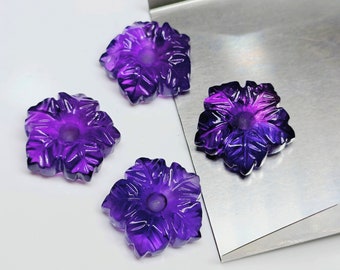 Könnte beinhalten: Vier violette Amethyst-Blumen-Schnitzereien, jede mit einem zentralen Loch, sind auf einer silbernen Oberfläche angeordnet.